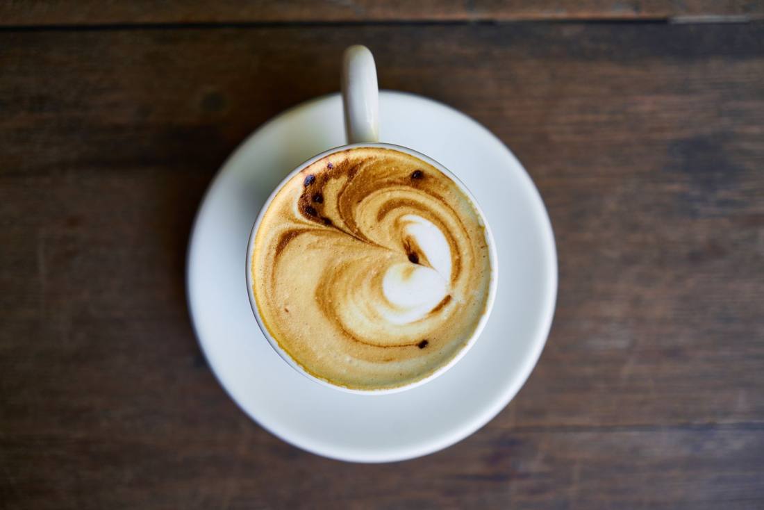 Top view of a coffee cup with intricate latte art on a white saucer.