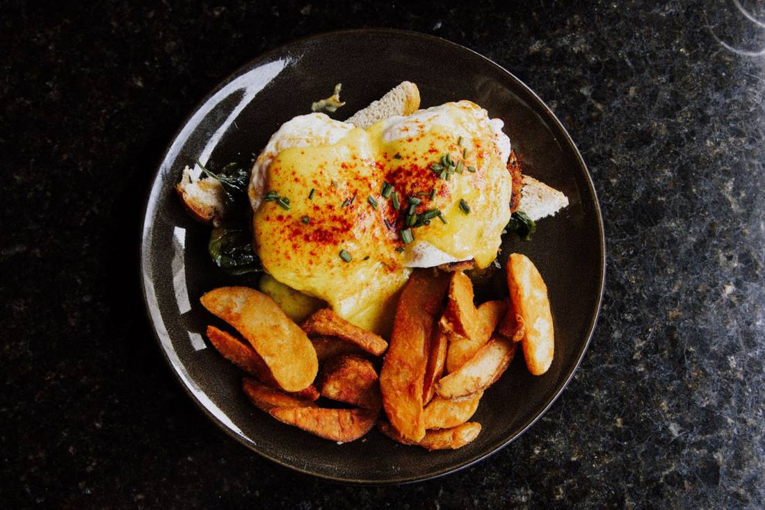 Delicious Eggs Benedict with creamy sauce and crispy potato wedges served on a dark plate.
