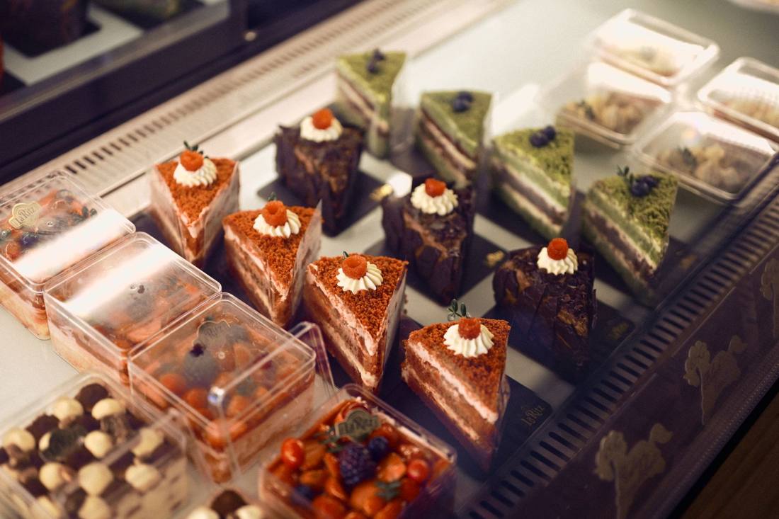 Vibrant cake slices including matcha and chocolate varieties on display at a patisserie.
