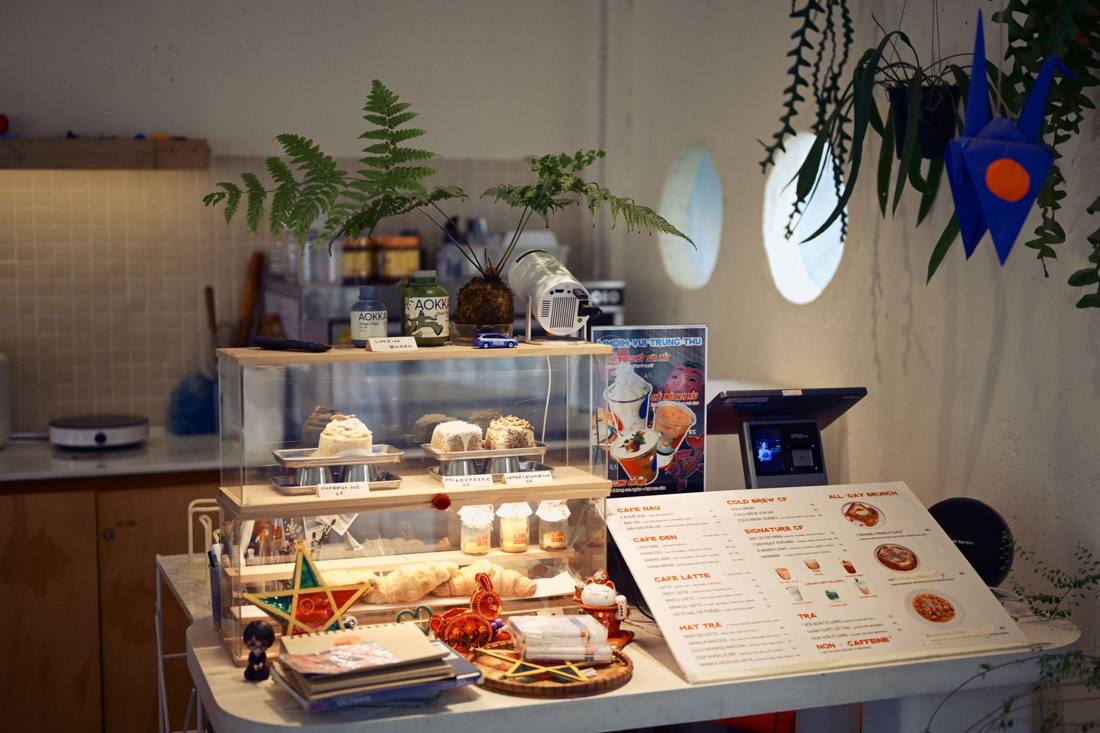 Cozy coffee shop interior with a pastry display, ferns, and a menu on the counter.